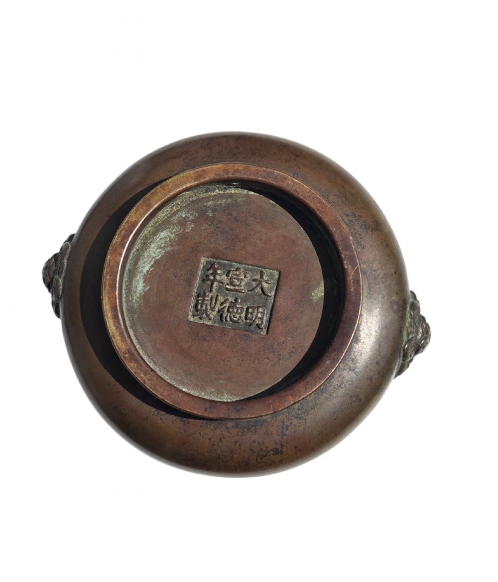 A cast bronze censer featuring a flared rim, compressed globular body, low circular foot, and cast relief taotie mask handles on the side. View XII