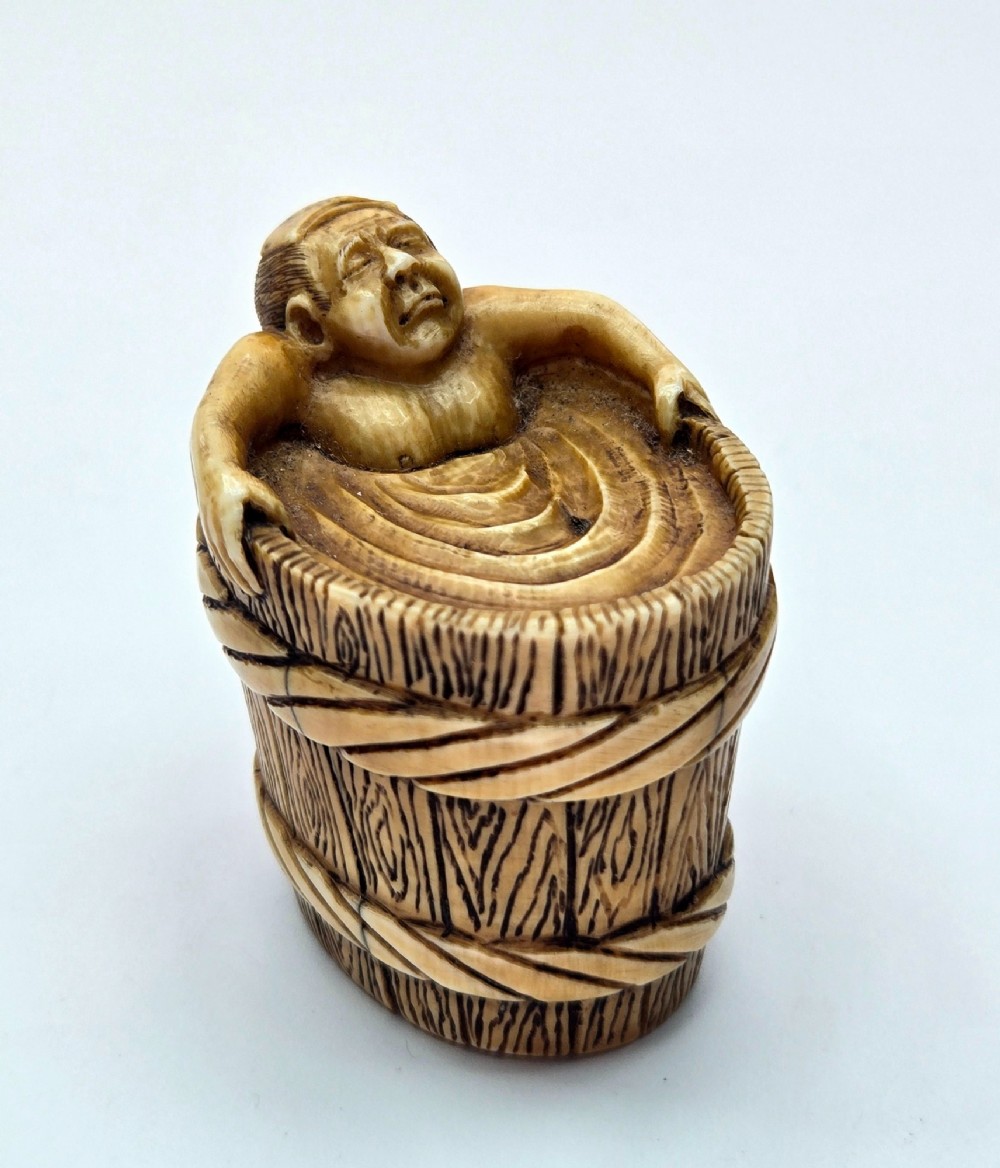 A small carved stag antler netsuke depicting a man sitting inside a wooden bath tub with carved water ripples. View II