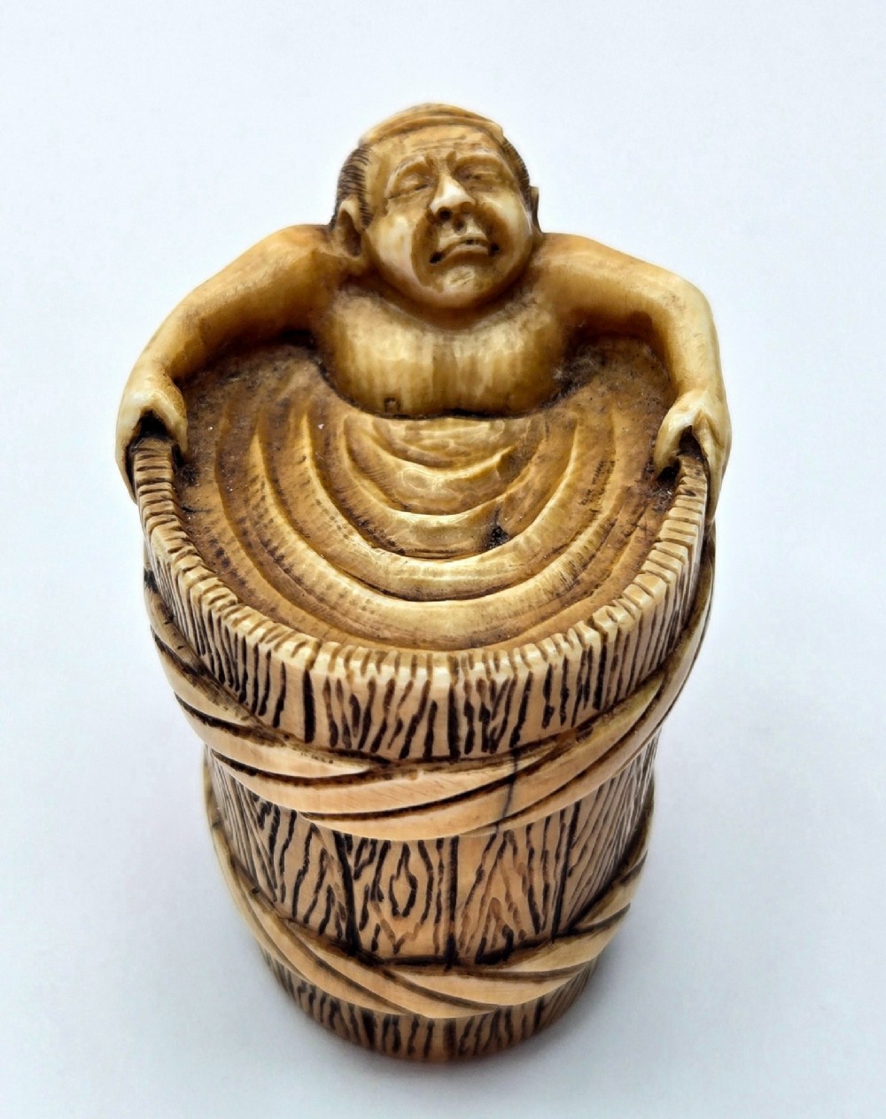 A small carved stag antler netsuke depicting a man sitting inside a wooden bath tub with carved water ripples. View III