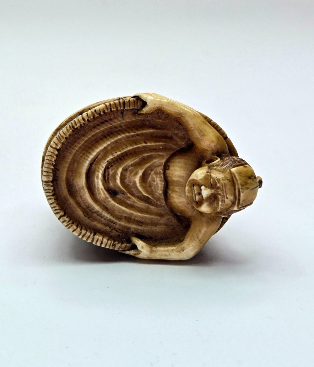 A small carved stag antler netsuke depicting a man sitting inside a wooden bath tub with carved water ripples. View VII