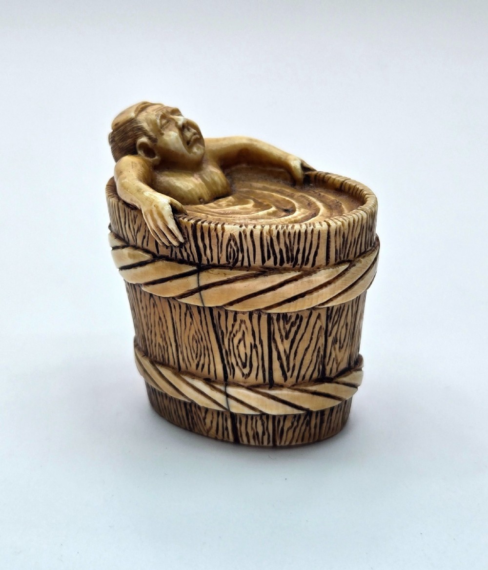A small carved stag antler netsuke depicting a man sitting inside a wooden bath tub with carved water ripples. View IX