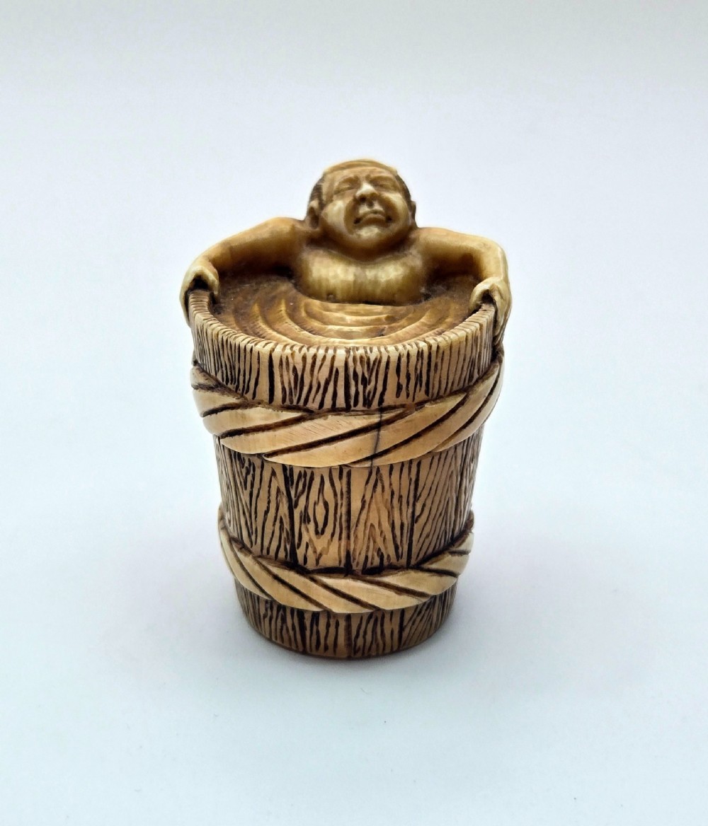 A small carved stag antler netsuke depicting a man sitting inside a wooden bath tub with carved water ripples. View X