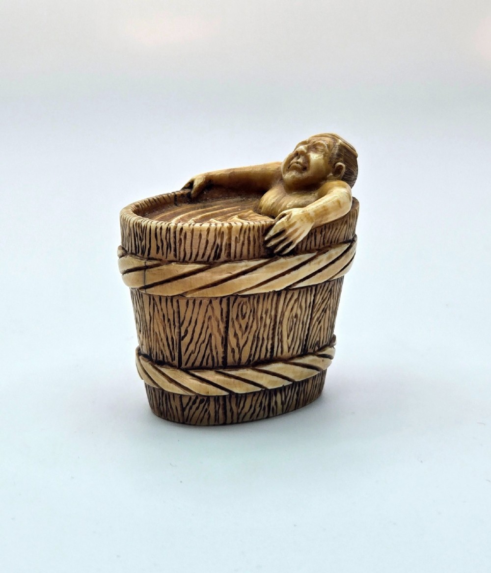 A small carved stag antler netsuke depicting a man sitting inside a wooden bath tub with carved water ripples. View XI