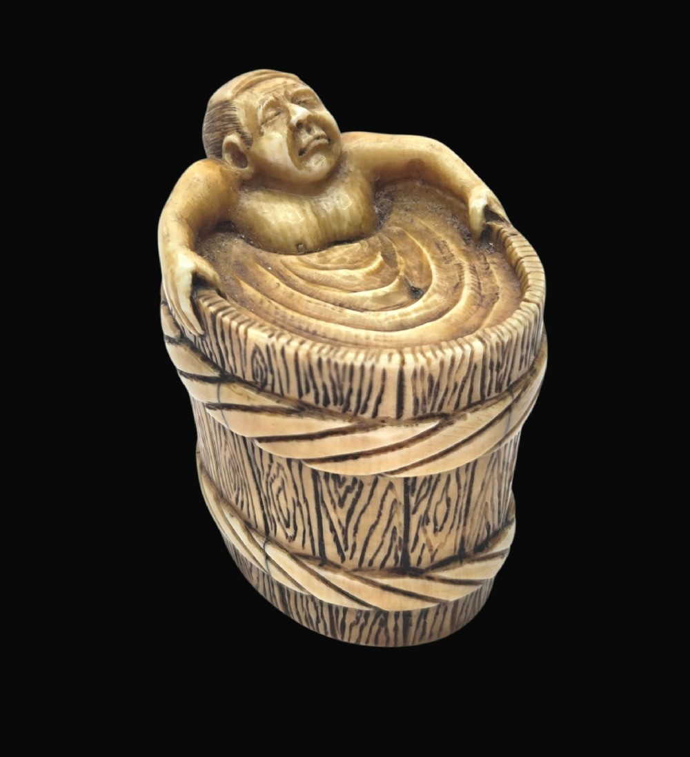 A small carved stag antler netsuke depicting a man sitting inside a wooden bath tub with carved water ripples. View XII