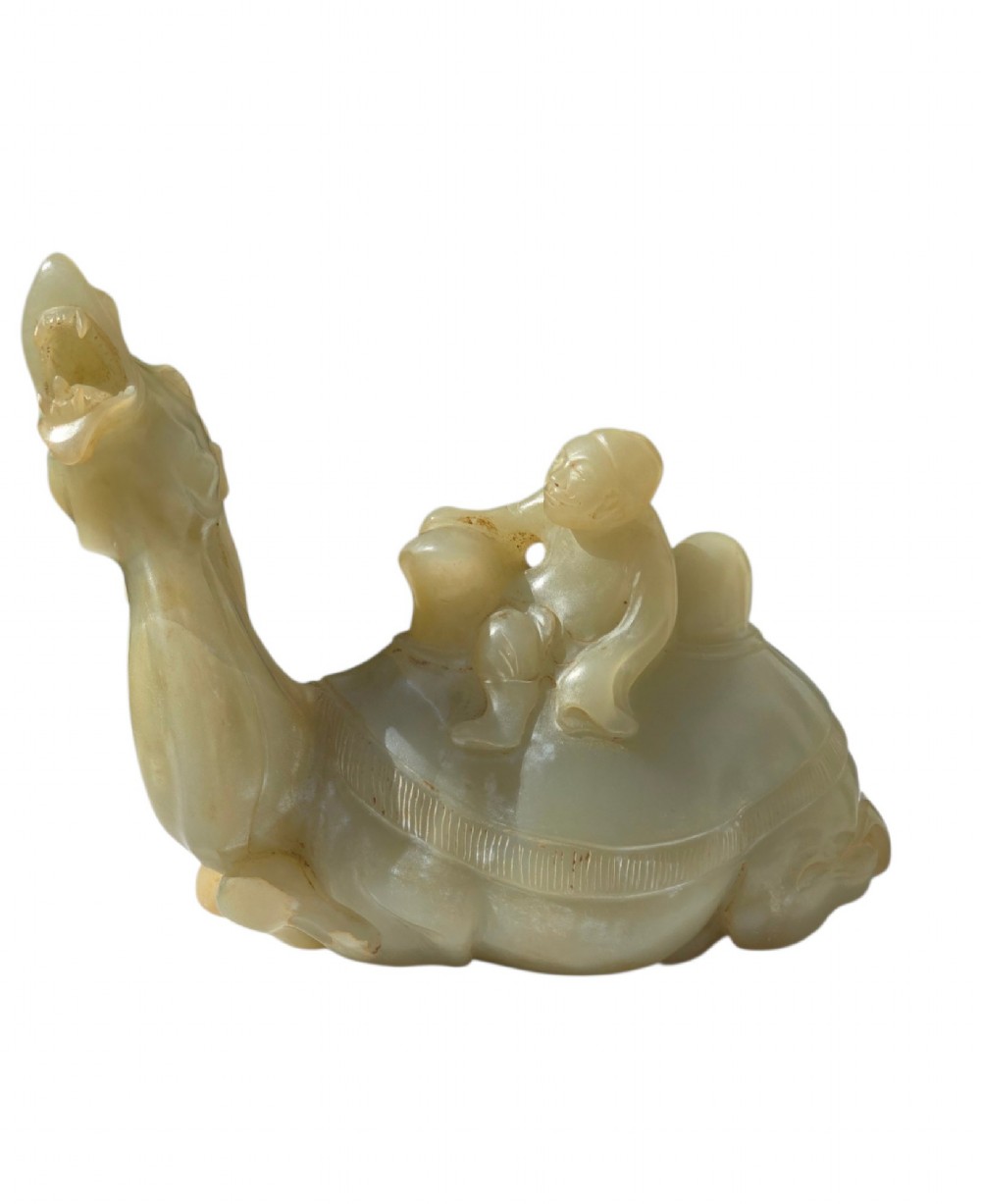 A carved pale green bowenite serpentine sculpture depicting a camel with its head raised, carrying a seated rider figure.