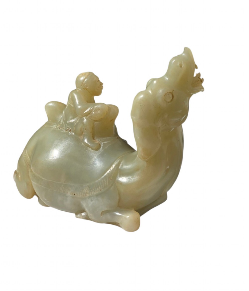 A carved pale green bowenite serpentine sculpture depicting a camel with its head raised, carrying a seated rider figure. View IV