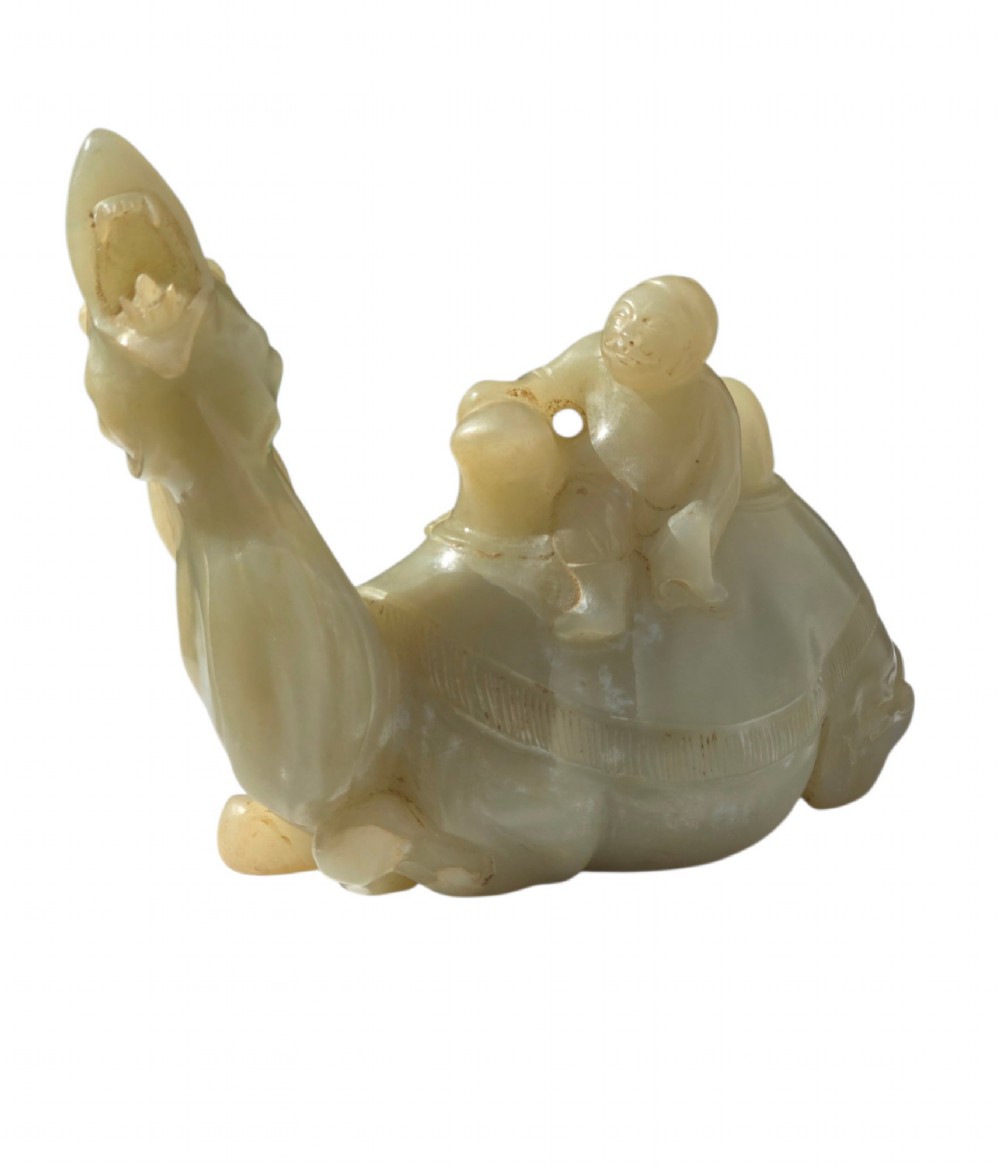 A carved pale green bowenite serpentine sculpture depicting a camel with its head raised, carrying a seated rider figure. View V