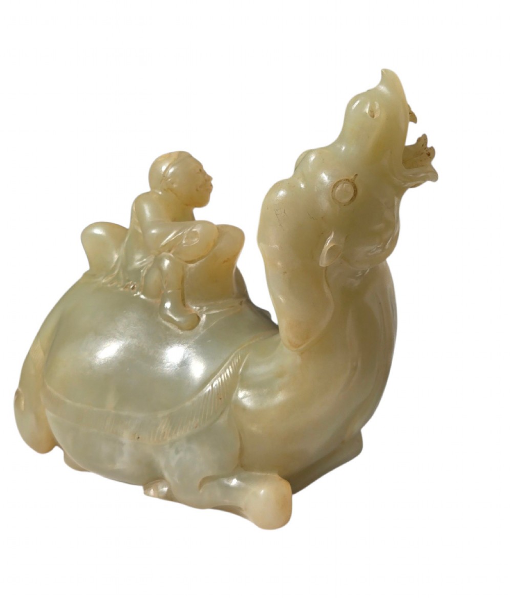 A carved pale green bowenite serpentine sculpture depicting a camel with its head raised, carrying a seated rider figure. View X