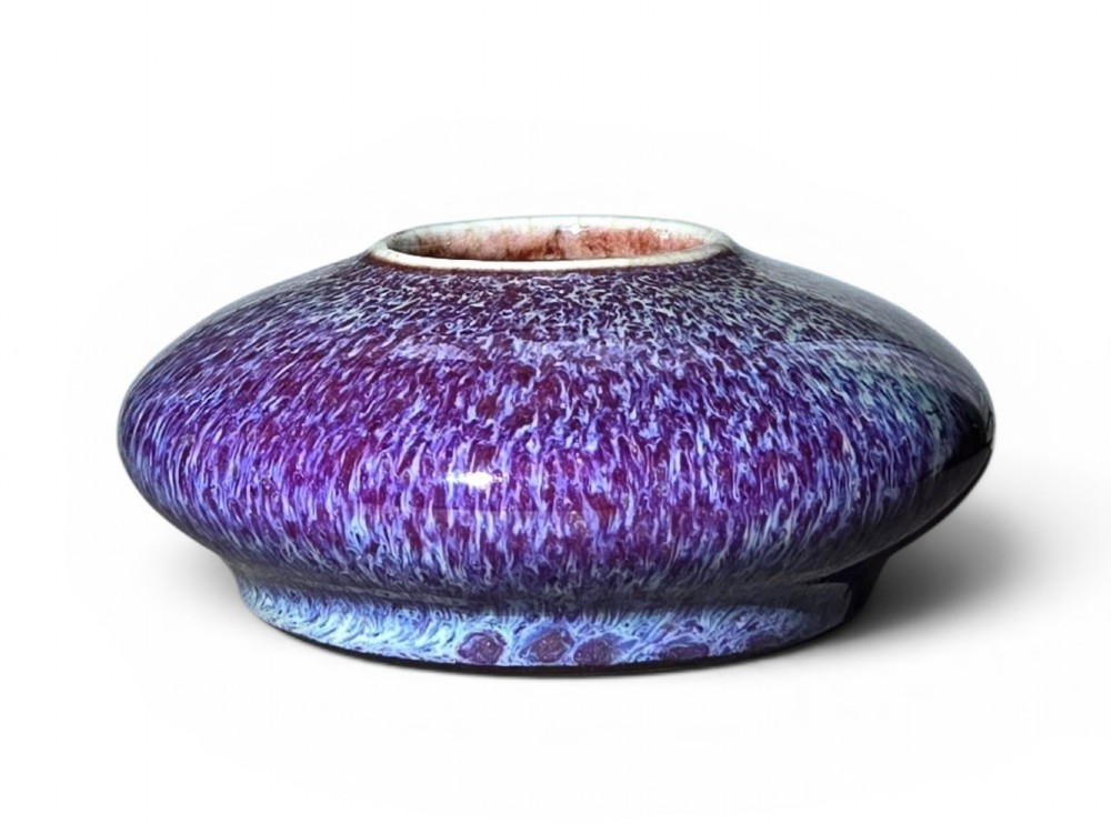 A compressed circular Chinese porcelain brush washer featuring a mottled purple and lavender blue flambe glaze.