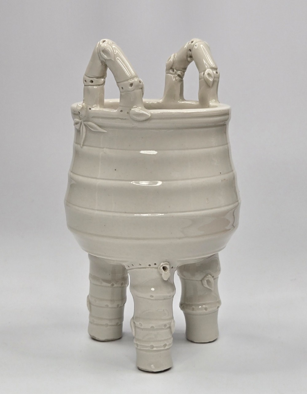 An off-white porcelain tripod censer featuring bamboo-node shaped legs, elevated loop handles, and subtle horizontal ridges across the body. View II