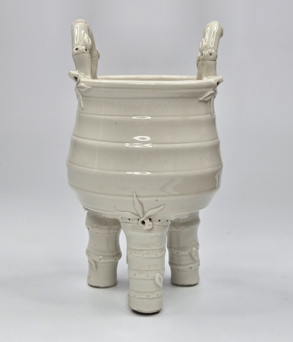 An off-white porcelain tripod censer featuring bamboo-node shaped legs, elevated loop handles, and subtle horizontal ridges across the body. View IV