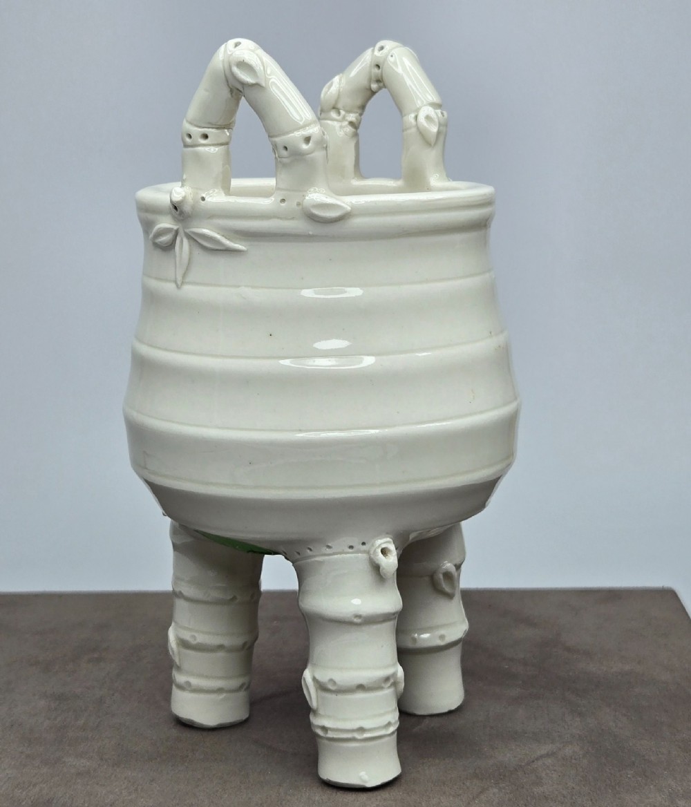 An off-white porcelain tripod censer featuring bamboo-node shaped legs, elevated loop handles, and subtle horizontal ridges across the body. View IX