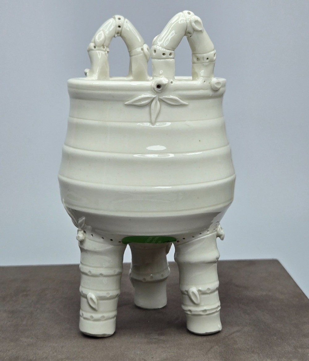 An off-white porcelain tripod censer featuring bamboo-node shaped legs, elevated loop handles, and subtle horizontal ridges across the body. View X