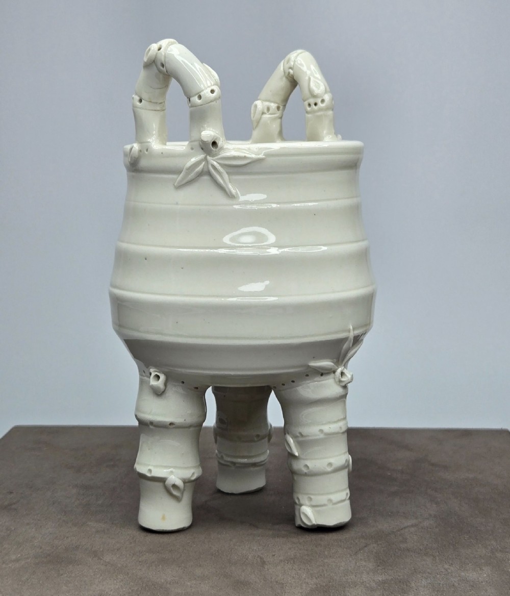 An off-white porcelain tripod censer featuring bamboo-node shaped legs, elevated loop handles, and subtle horizontal ridges across the body. View XIII