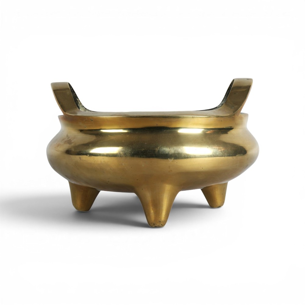 A heavy gold-toned cast bronze tripod censer featuring two upright loop handles and conical feet.
