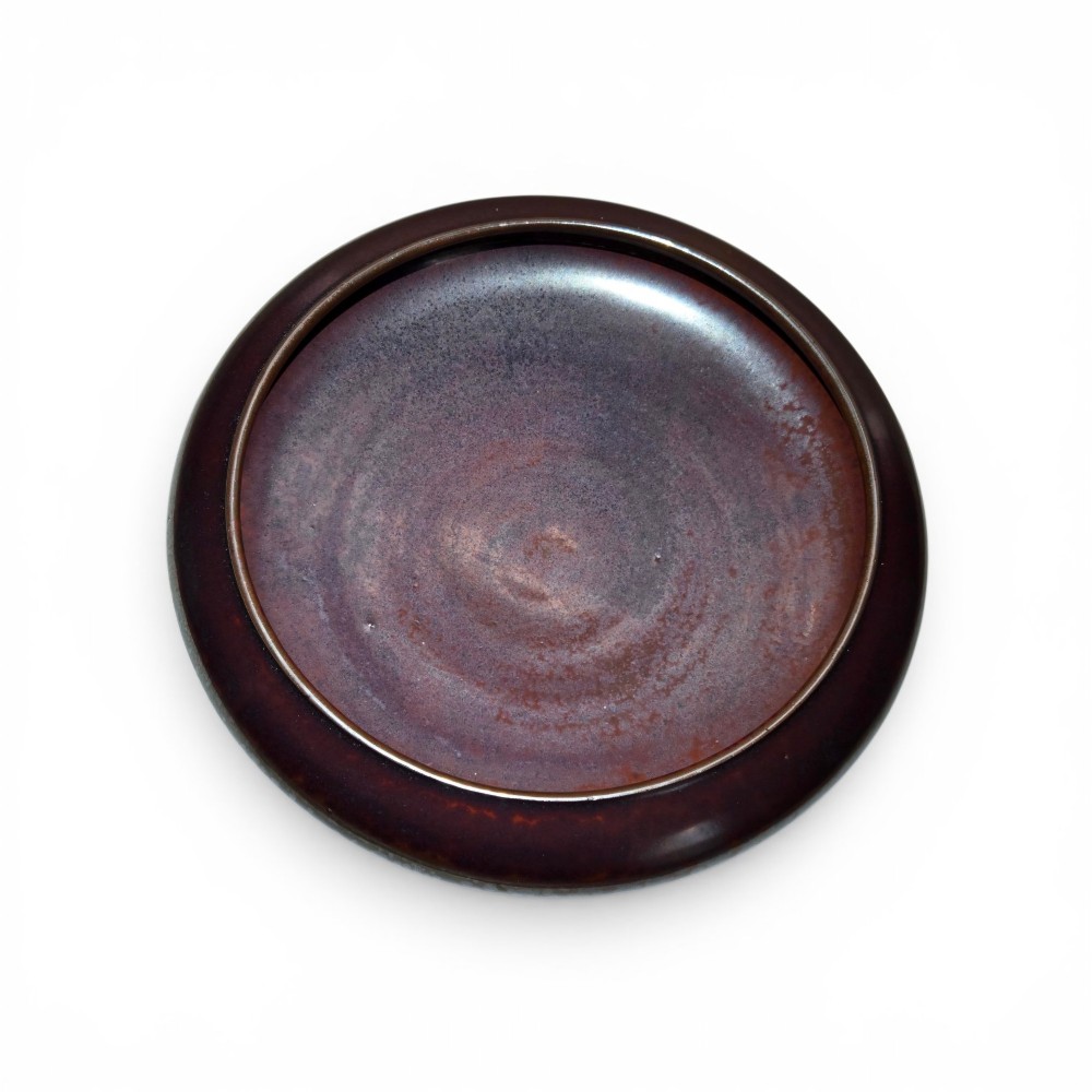 A low compressed circular ceramic brush washer featuring a dark reddish-brown iron rust glaze with subtle metallic speckling. View V