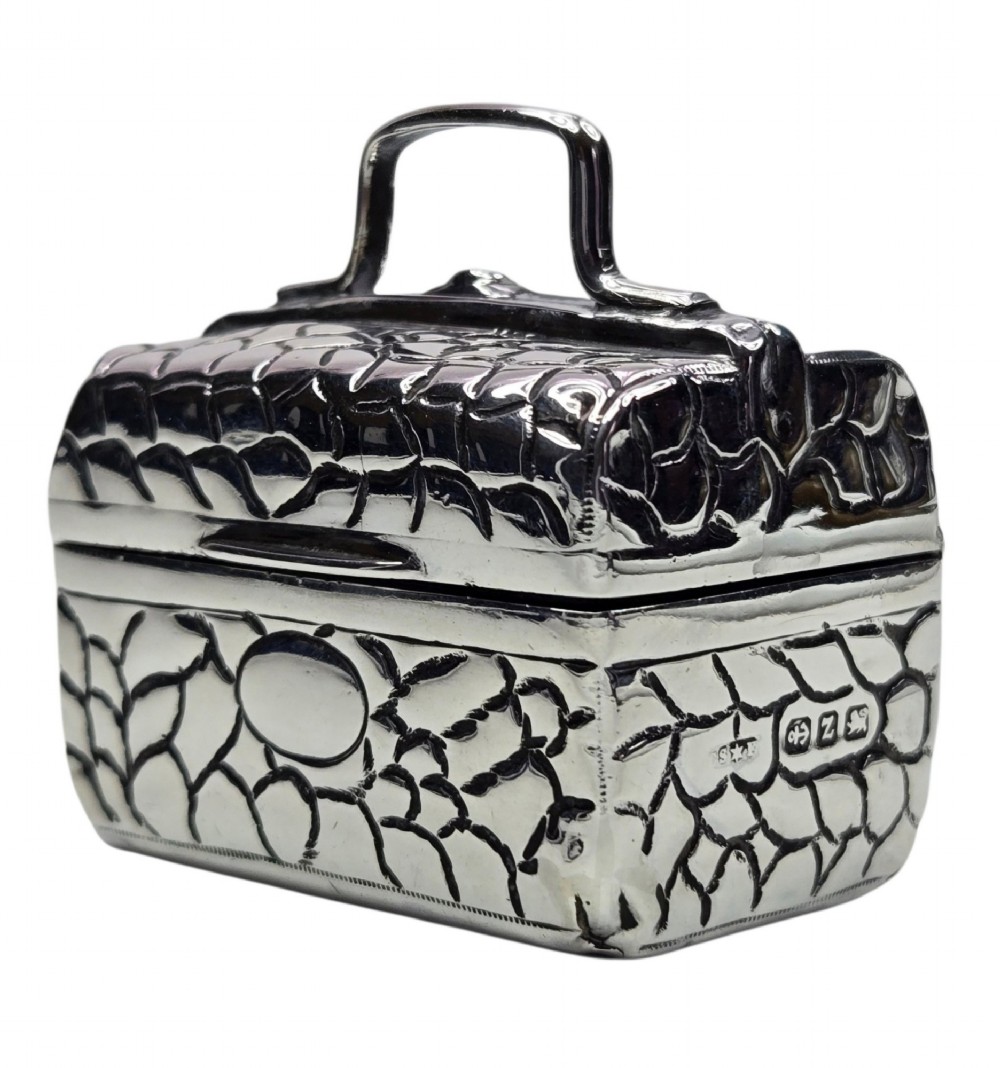 A late Victorian sterling silver novelty box crafted in the form of a miniature trunk with embossed crocodile skin texture and a top carrying handle.