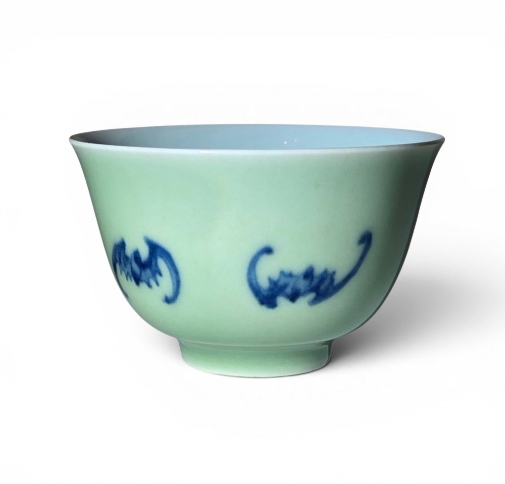 A small Chinese celadon green glazed porcelain cup decorated with underglaze blue bat motifs around the exterior.