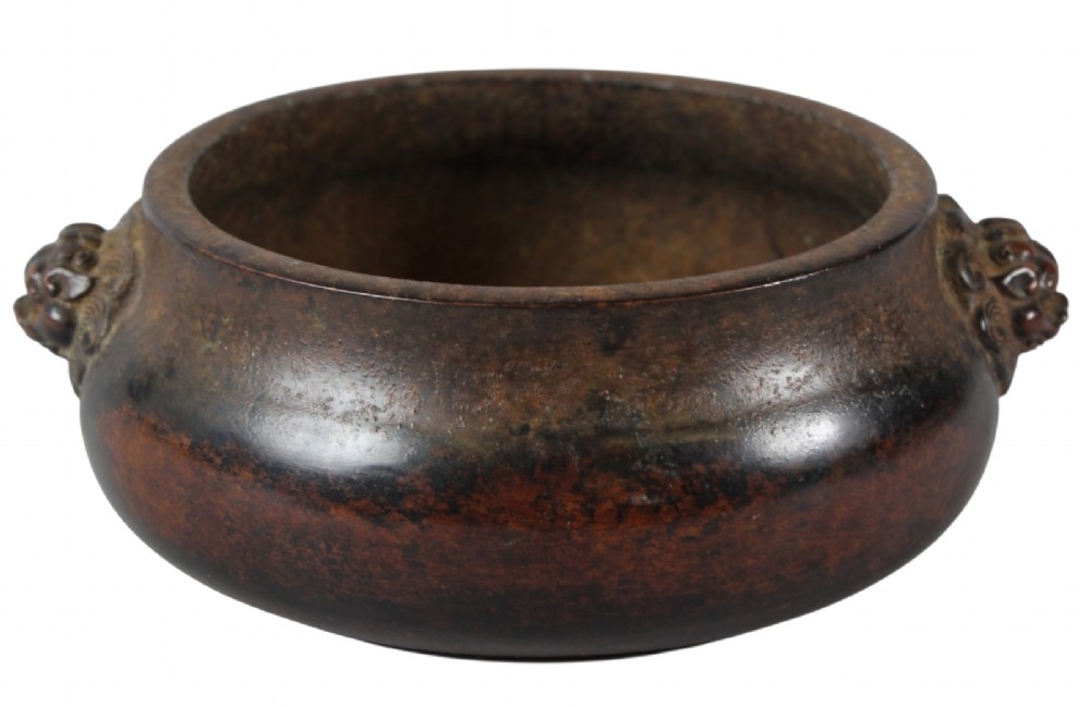 A heavy dark brown cast bronze incense burner featuring a low compressed circular form decorated with relief beast mask handles. View VI