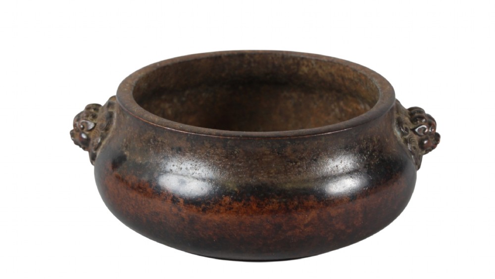 A heavy dark brown cast bronze incense burner featuring a low compressed circular form decorated with relief beast mask handles. View VIII