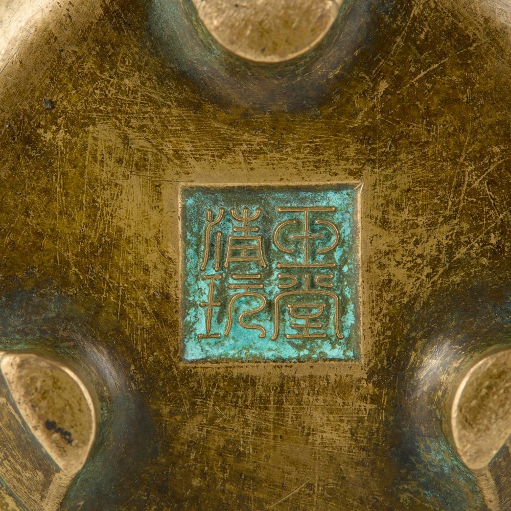 Underside view of a heavy bronze tripod censer displaying three short feet and a square recessed seal mark filled with turquoise oxidisation.