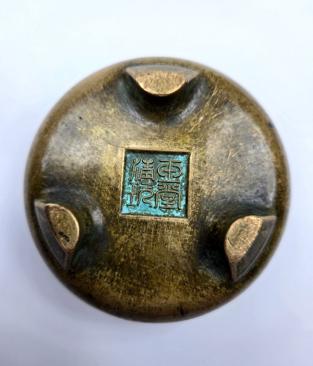 Underside view of a heavy bronze tripod censer displaying three short feet and a square recessed seal mark filled with turquoise oxidisation. View IV