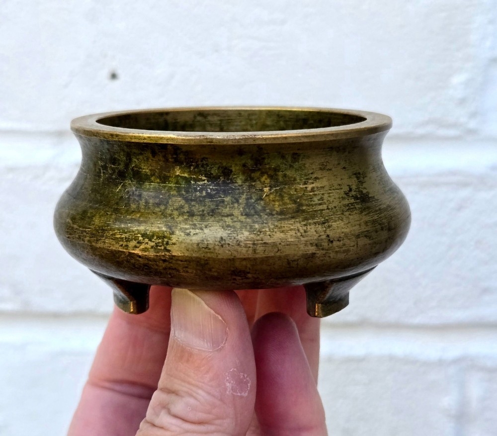 Underside view of a heavy bronze tripod censer displaying three short feet and a square recessed seal mark filled with turquoise oxidisation. View V