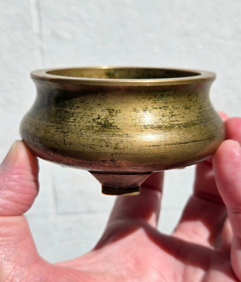 Underside view of a heavy bronze tripod censer displaying three short feet and a square recessed seal mark filled with turquoise oxidisation. View VII