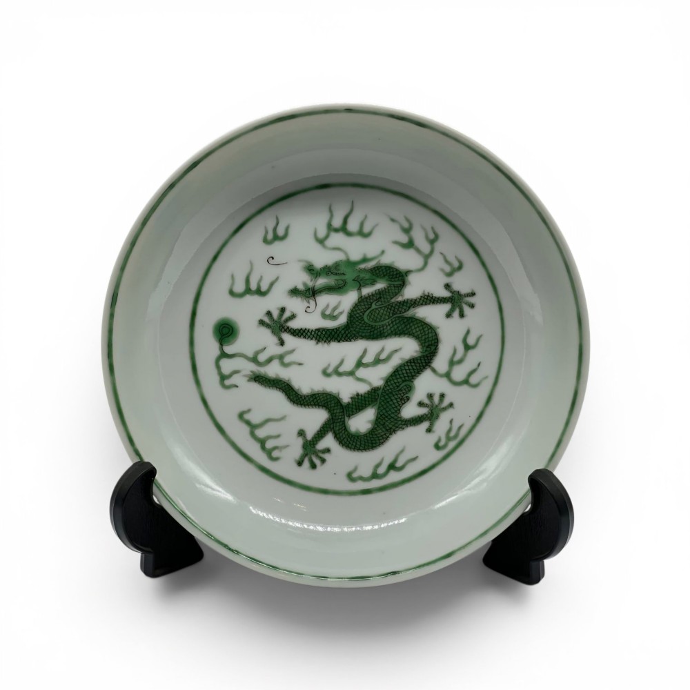 A circular white porcelain dish featuring a central green five-clawed dragon painted in overglaze enamel amidst stylised flames.