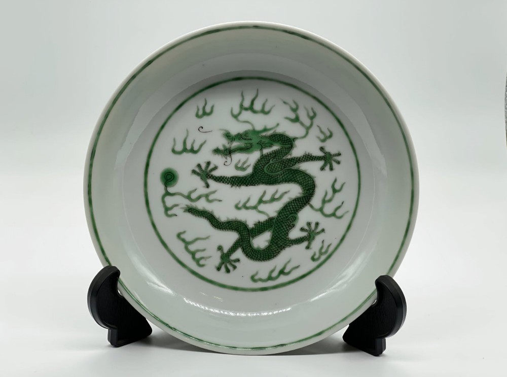 A circular white porcelain dish featuring a central green five-clawed dragon painted in overglaze enamel amidst stylised flames. View III