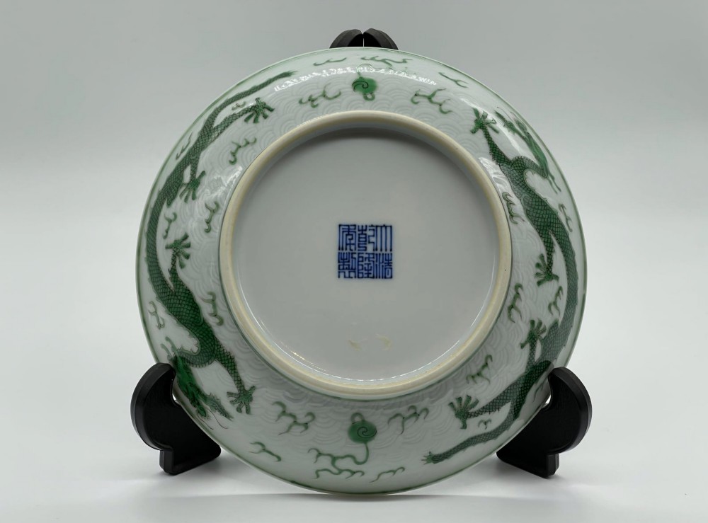 A circular white porcelain dish featuring a central green five-clawed dragon painted in overglaze enamel amidst stylised flames. View IV