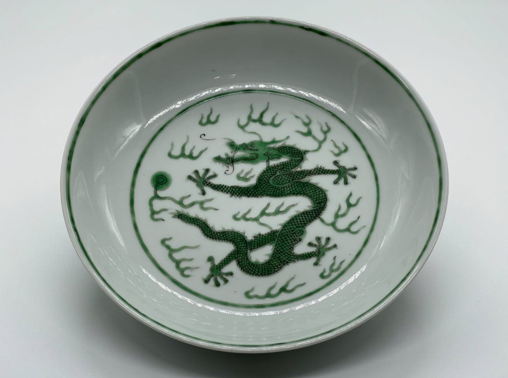 A circular white porcelain dish featuring a central green five-clawed dragon painted in overglaze enamel amidst stylised flames. View V