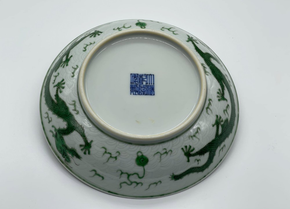 A circular white porcelain dish featuring a central green five-clawed dragon painted in overglaze enamel amidst stylised flames. View VI