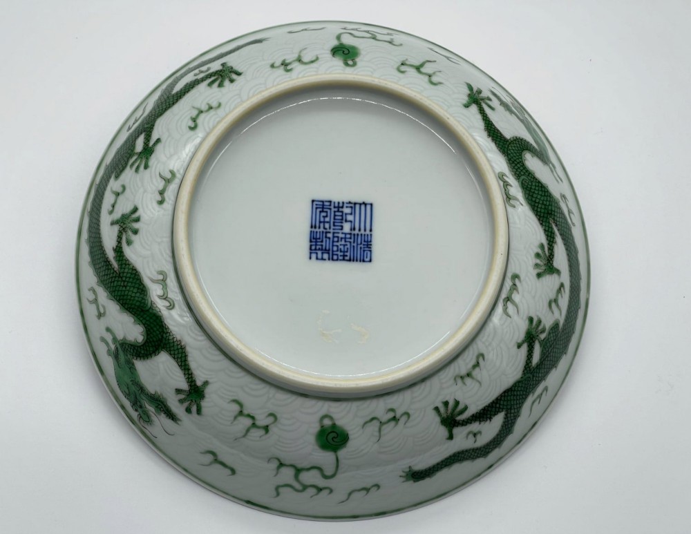 A circular white porcelain dish featuring a central green five-clawed dragon painted in overglaze enamel amidst stylised flames. View VII