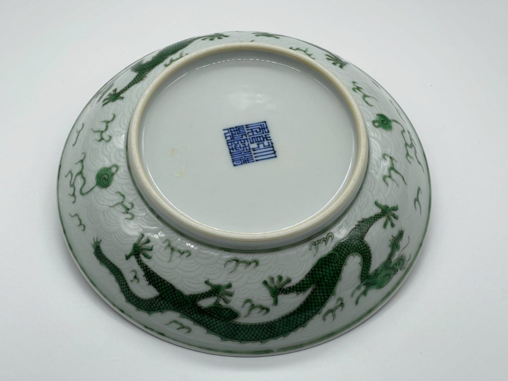 A circular white porcelain dish featuring a central green five-clawed dragon painted in overglaze enamel amidst stylised flames. View IX