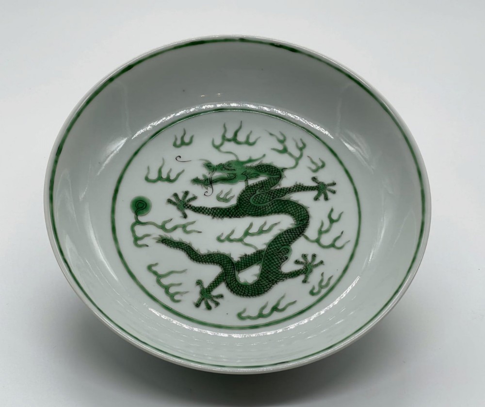 A circular white porcelain dish featuring a central green five-clawed dragon painted in overglaze enamel amidst stylised flames. View X