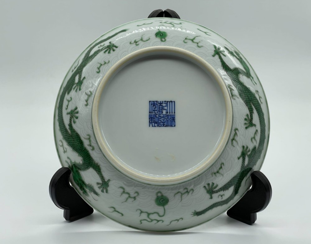 A circular white porcelain dish featuring a central green five-clawed dragon painted in overglaze enamel amidst stylised flames. View XII