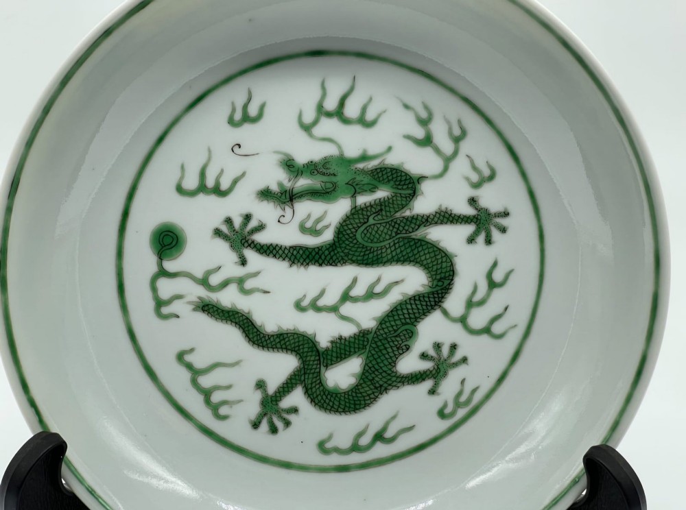 A circular white porcelain dish featuring a central green five-clawed dragon painted in overglaze enamel amidst stylised flames. View XIII