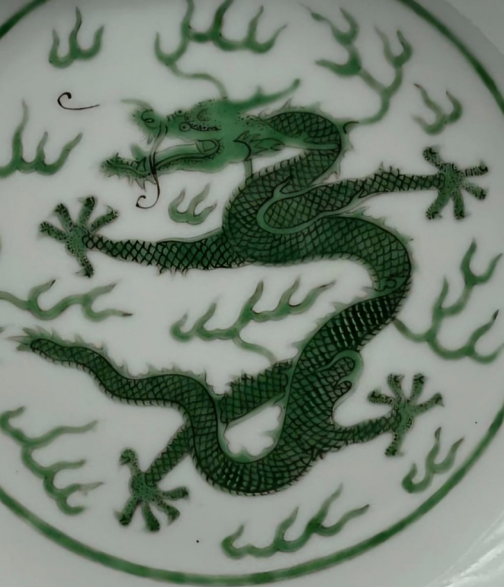 A circular white porcelain dish featuring a central green five-clawed dragon painted in overglaze enamel amidst stylised flames. View XIV