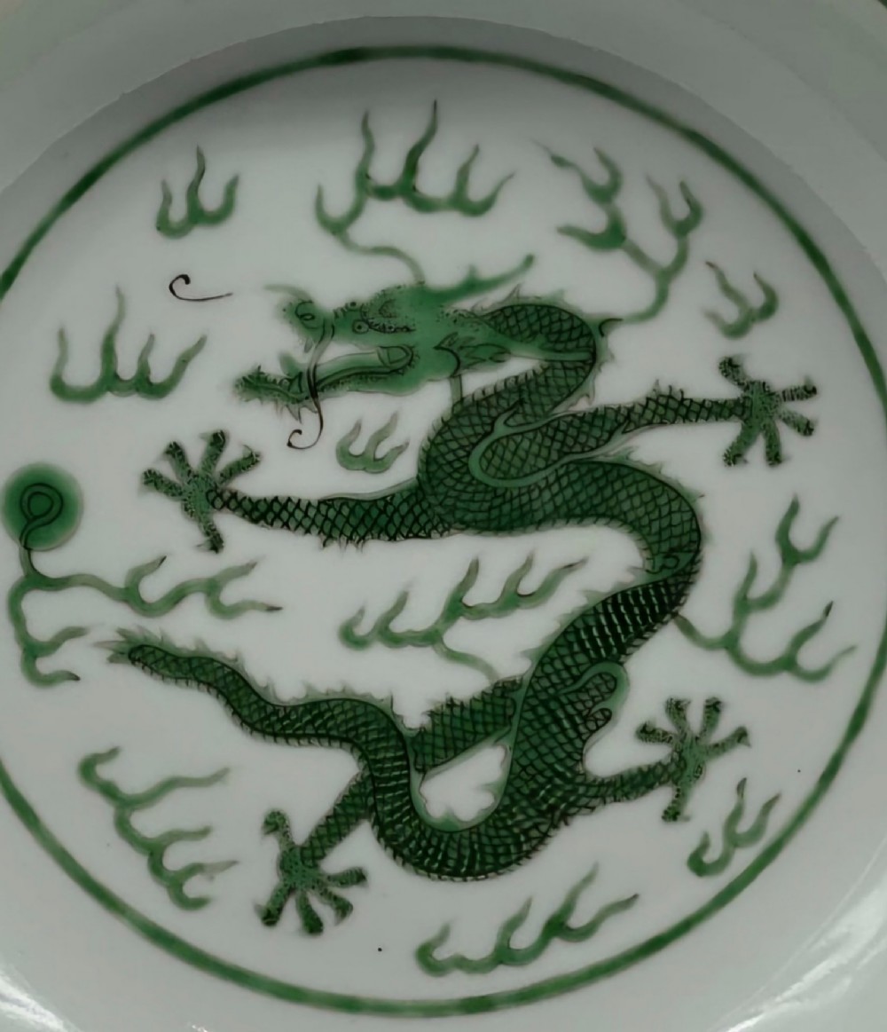 A circular white porcelain dish featuring a central green five-clawed dragon painted in overglaze enamel amidst stylised flames. View XV