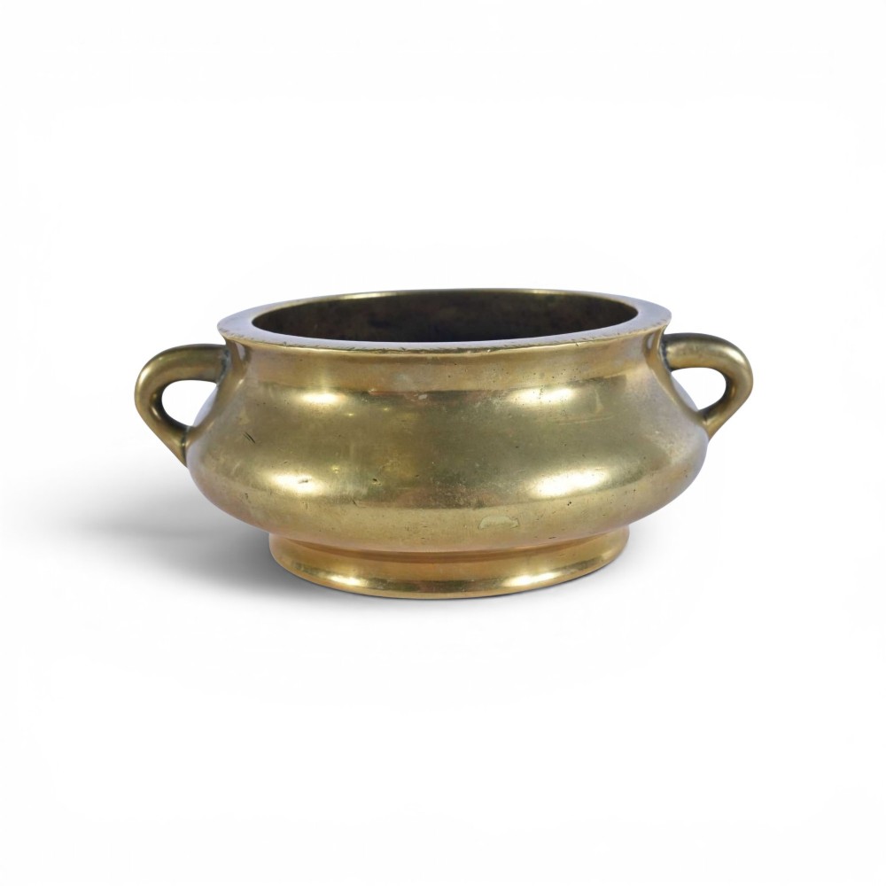 An 18th-century cast bronze incense burner featuring a compressed rounded body, flared rim, two loop handles, and a burnished golden patinated finish.
