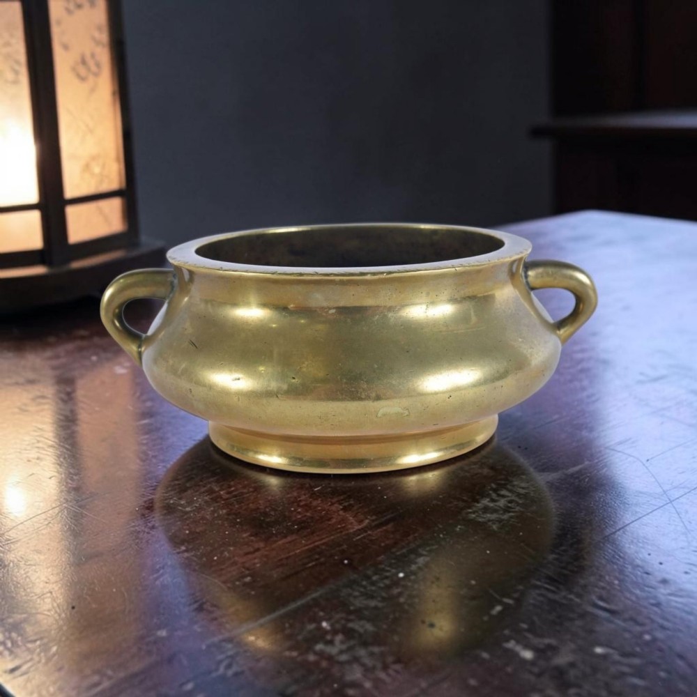 An 18th-century cast bronze incense burner featuring a compressed rounded body, flared rim, two loop handles, and a burnished golden patinated finish. View X