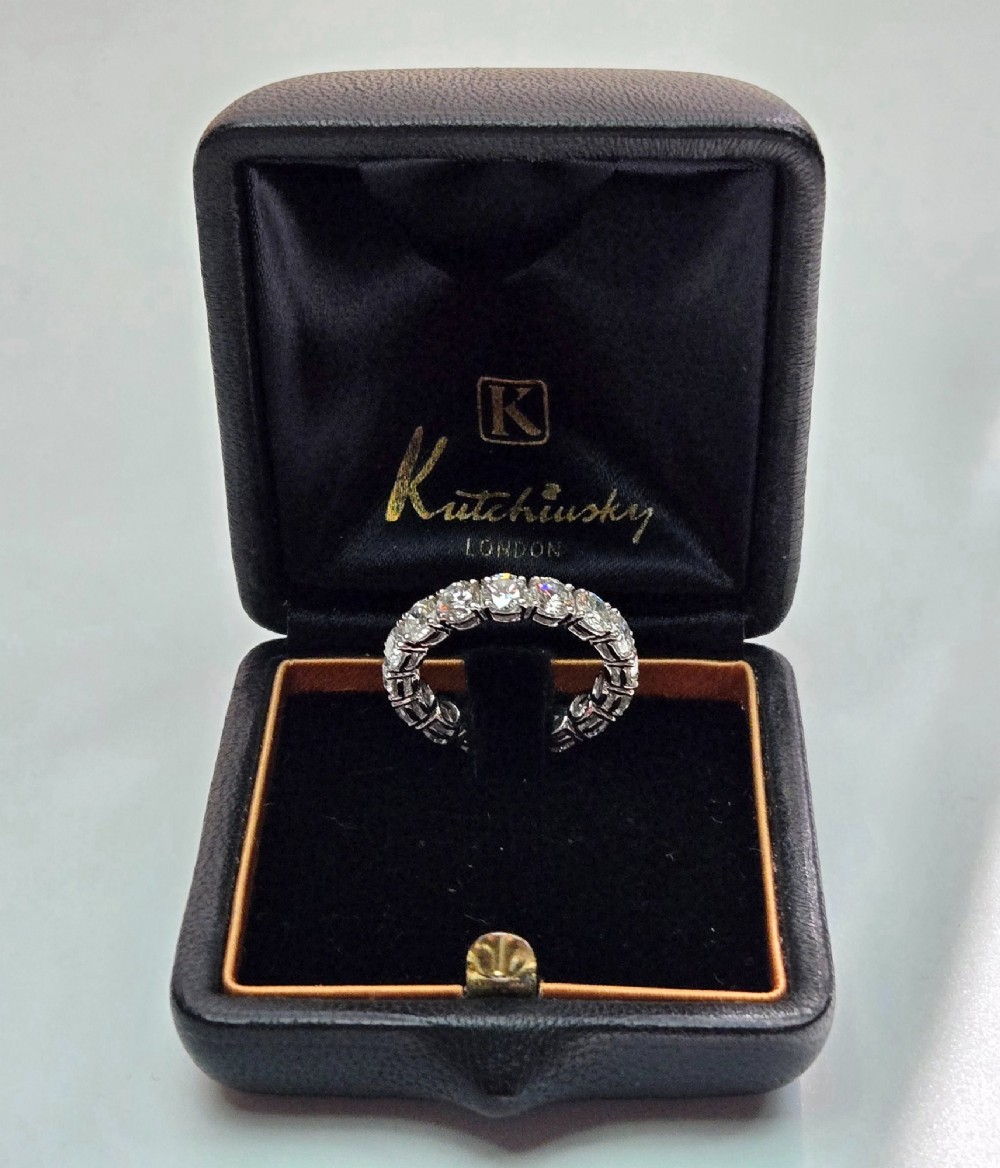 A platinum full eternity ring set with round brilliant diamonds, displayed inside its original black leather Kutchinsky box. View II
