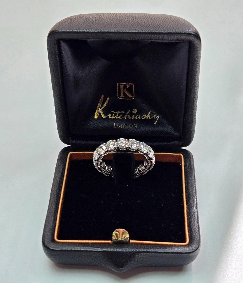 A platinum full eternity ring set with round brilliant diamonds, displayed inside its original black leather Kutchinsky box. View IX
