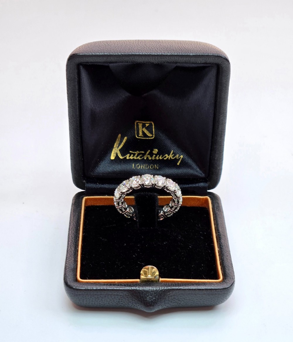 A platinum full eternity ring set with round brilliant diamonds, displayed inside its original black leather Kutchinsky box. View X