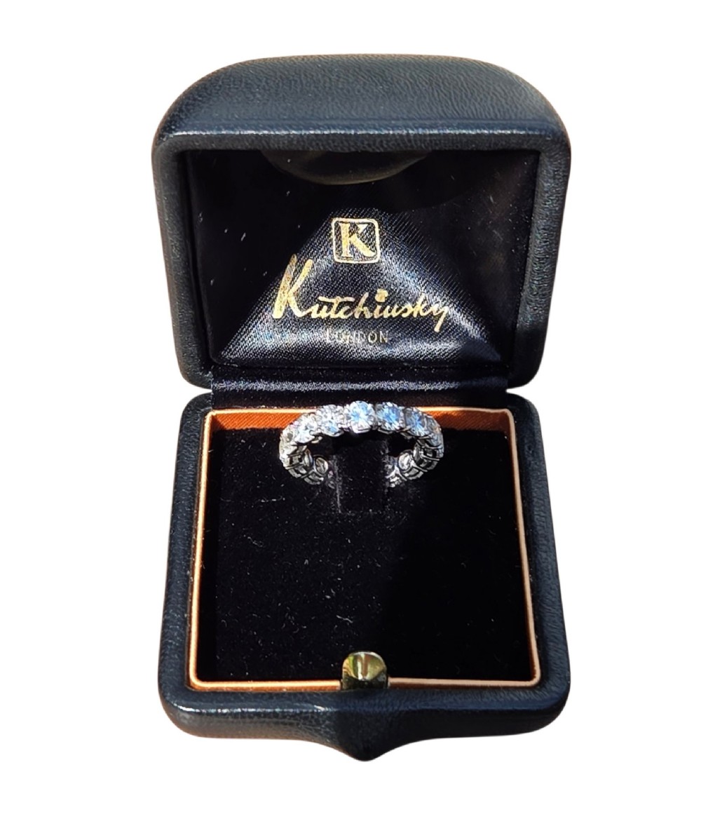 A platinum full eternity ring set with round brilliant diamonds, displayed inside its original black leather Kutchinsky box. View XIV