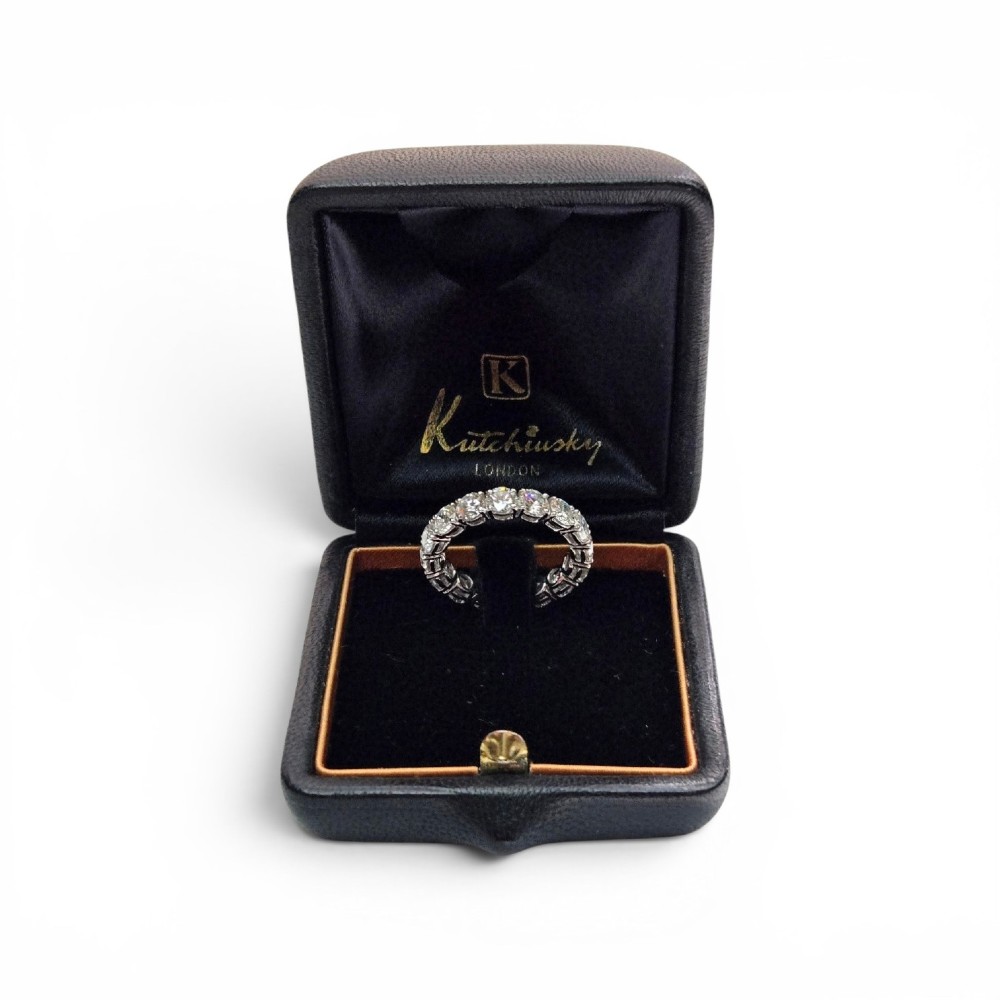 A platinum full eternity ring set with round brilliant diamonds, displayed inside its original black leather Kutchinsky box. View XV