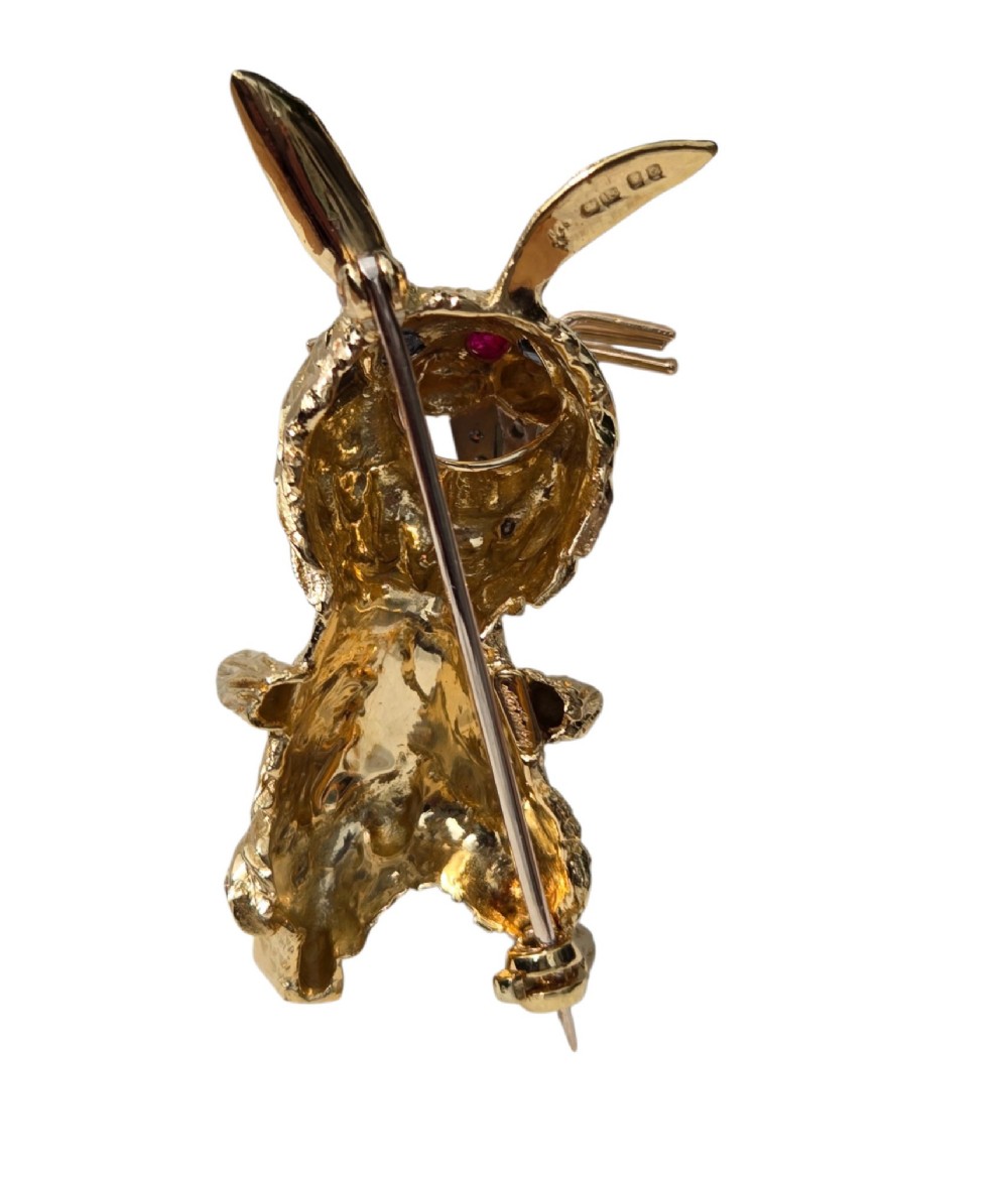 An 18ct yellow gold rabbit brooch showcasing textured fur detailing, a ruby nose, diamond-set teeth, and sapphire eyes. View IV
