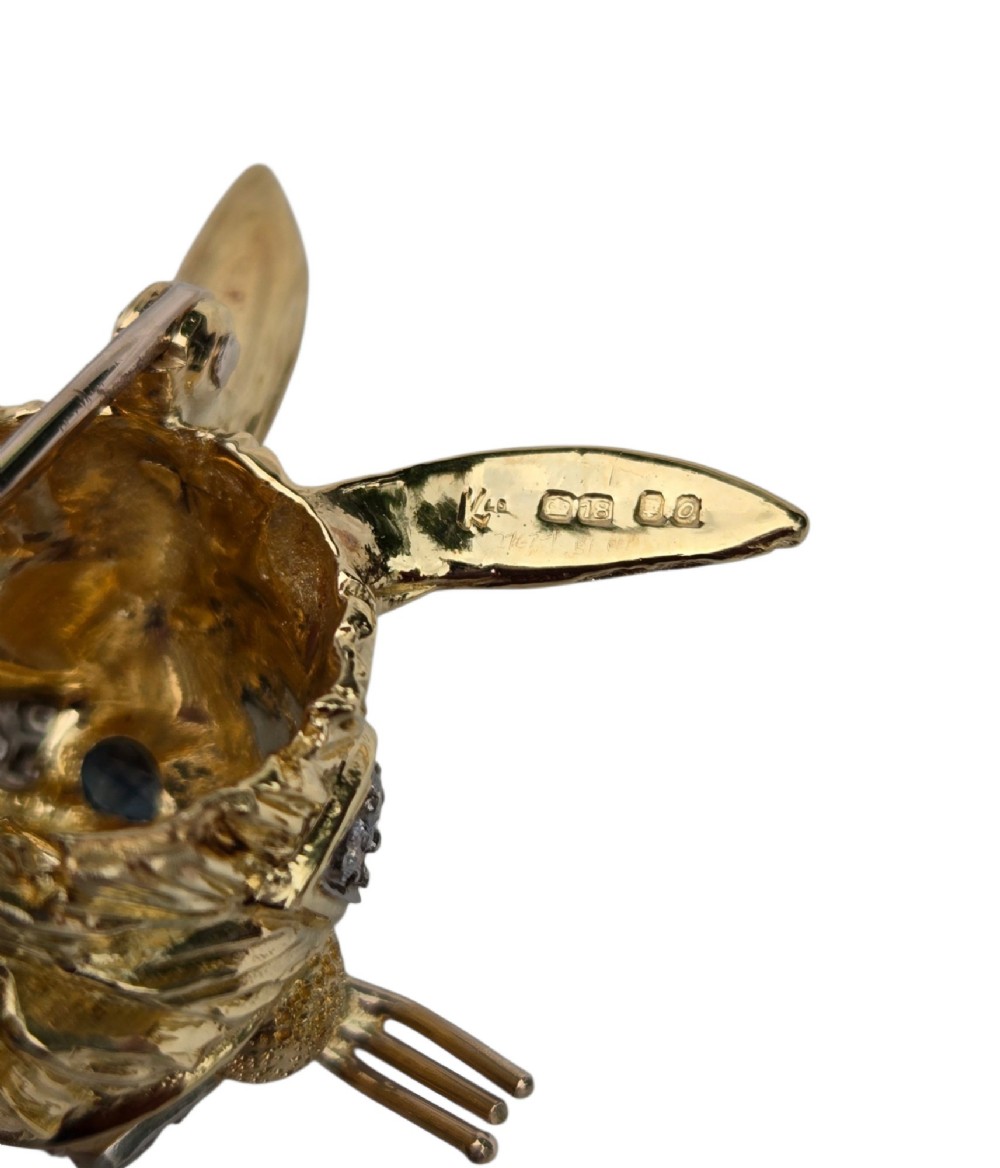 An 18ct yellow gold rabbit brooch showcasing textured fur detailing, a ruby nose, diamond-set teeth, and sapphire eyes. View V