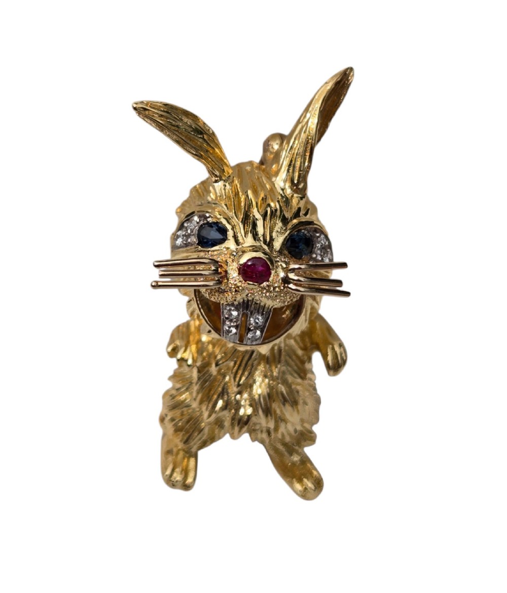 An 18ct yellow gold rabbit brooch showcasing textured fur detailing, a ruby nose, diamond-set teeth, and sapphire eyes. View VII